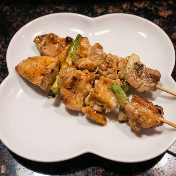 Two skewers of grilled chicken and scallions, glistening with sauce, on a white plate.
