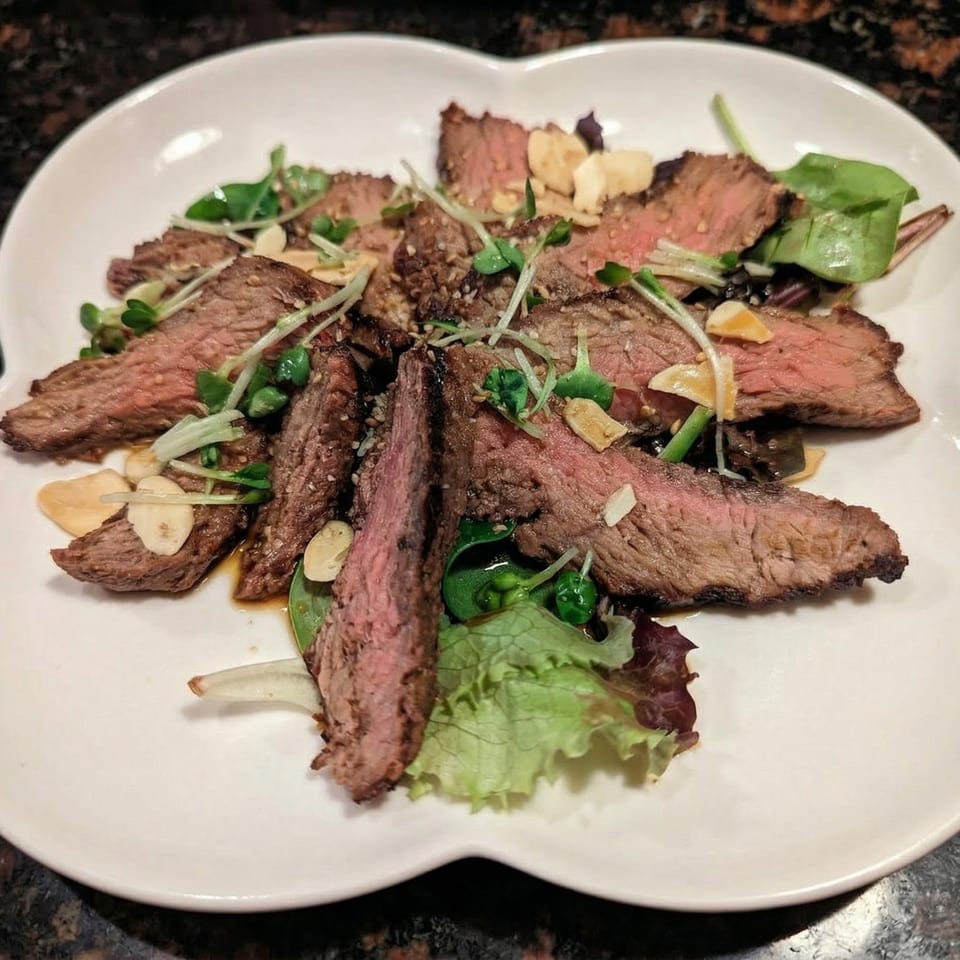 Sliced medium-rare steak with microgreens, garlic, and sesame seeds on a white plate.
